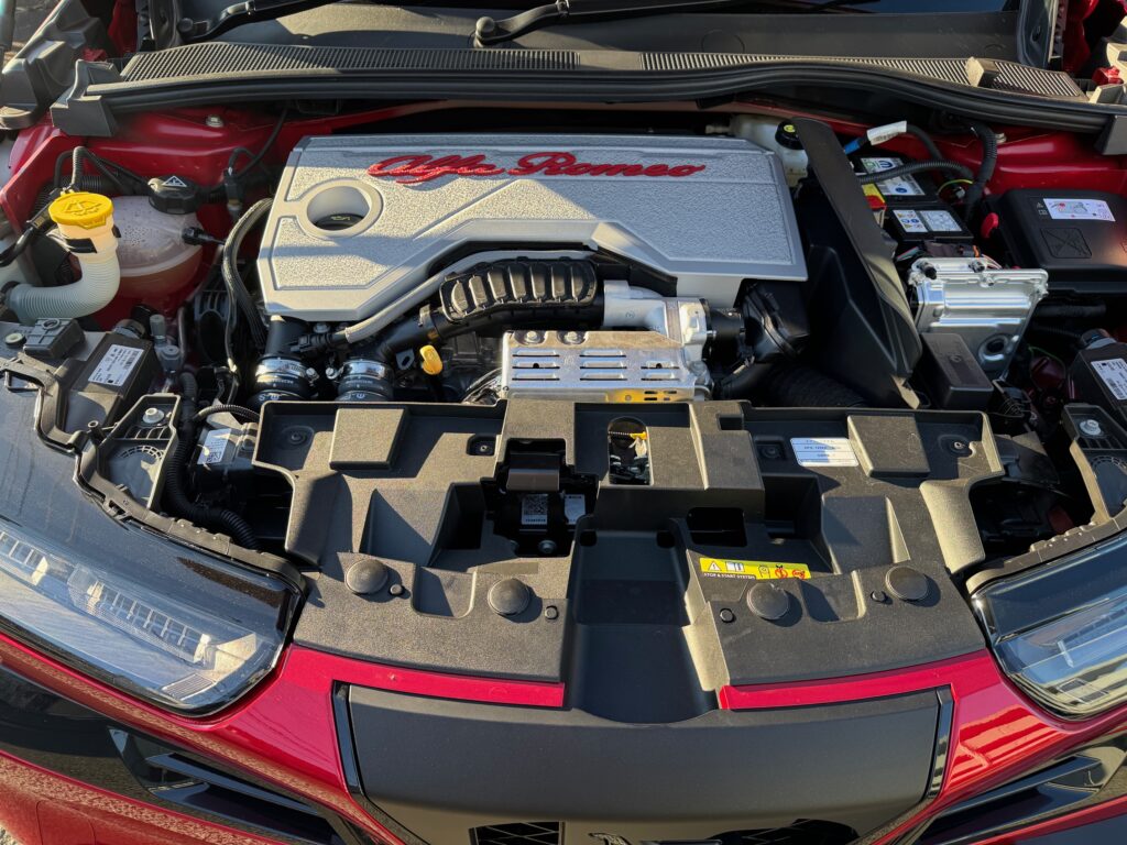 新型 アルファロメオ ジュニア イブリダ のエンジンルームに装着された、テクスチャ加工のシルバーエンジンヘッドカバー。深紅のロゴは歴代名機へのオマージュを表現し、UNLIMITEDなデザインと品質を追求した逸品パーツ。